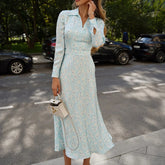 A woman in a light blue, floral satin dress standing on a street with cars in the background