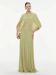 Model wearing a light green cape-overlay maxi dress on a white background, showing soft drape at the neckline and a slim silhouette.