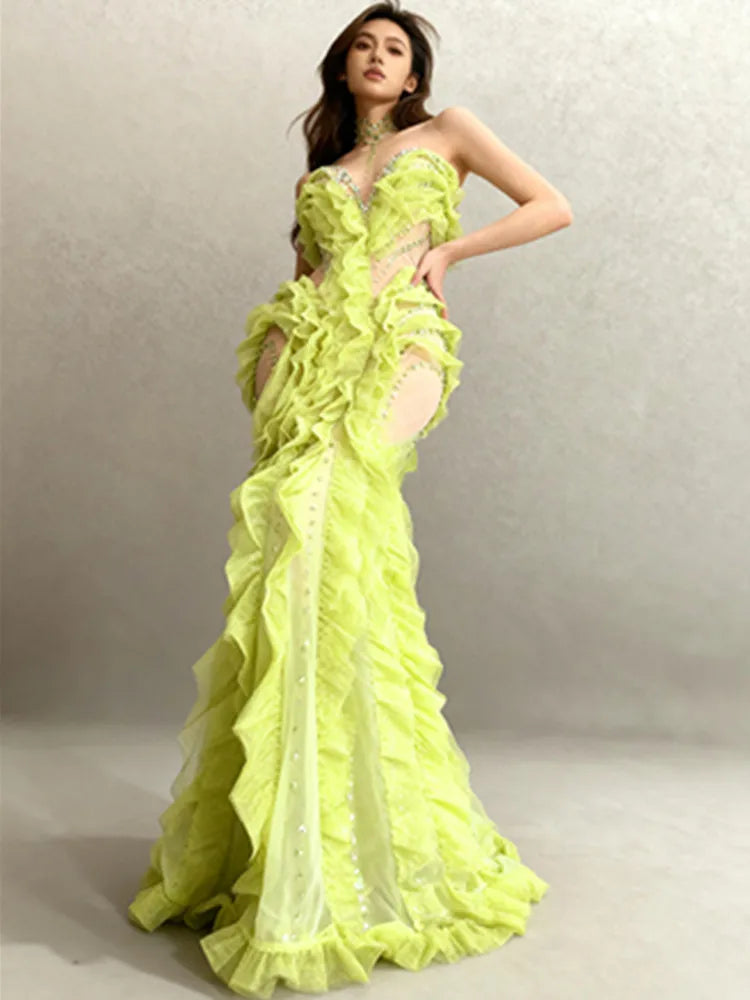 Model in a lime green floor-length gown with cascading ruffles and crystal detailing, posing in a studio against a neutral backdrop.