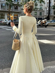 Woman in a gngham long sleeve midi dress in soft girl aesthetic back view holding an ice cream cone on a city street.
