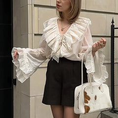 Woman wearing a loose fit long sleeve white office blouse for juniors and casual looksand black shorts, holding a cowhide patterned handbag.