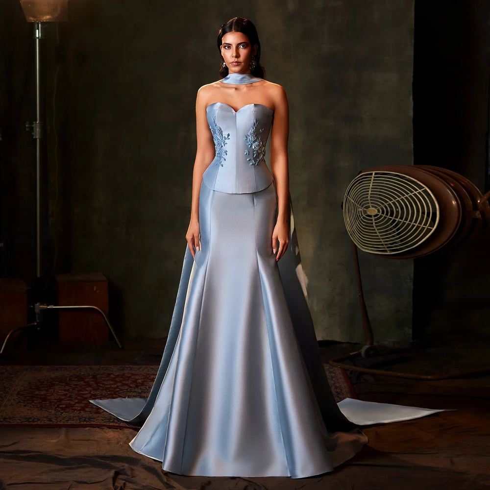Woman in a light blue evening gown standing in a dimly lit room with a vintage fan.