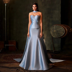 Woman in a light blue evening gown standing in a dimly lit room with a vintage fan.