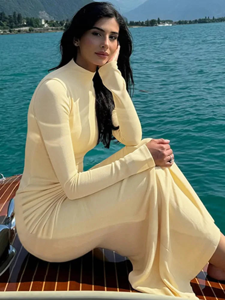 A woman wearing a yellow ruched maxi dress with a half high collar and metal decoration.