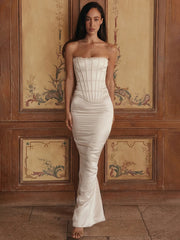 A woman wearing a minimalist white gown perfect for bridal or formal events, standing against a decorative wooden wall.