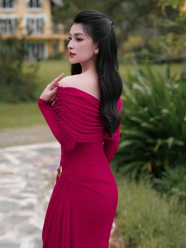 Woman in a modern sculpted red evening gown with a bold neckline for special eventsposing outdoors with greenery in the background