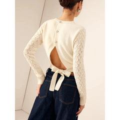 Woman wearing ribbed knit sweater with open back bow tie and pearl buttons