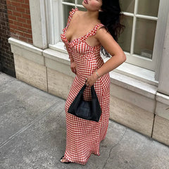 Woman in a Open back red check print maxi dress styled for vacations and picnics standing on a sidewalk.