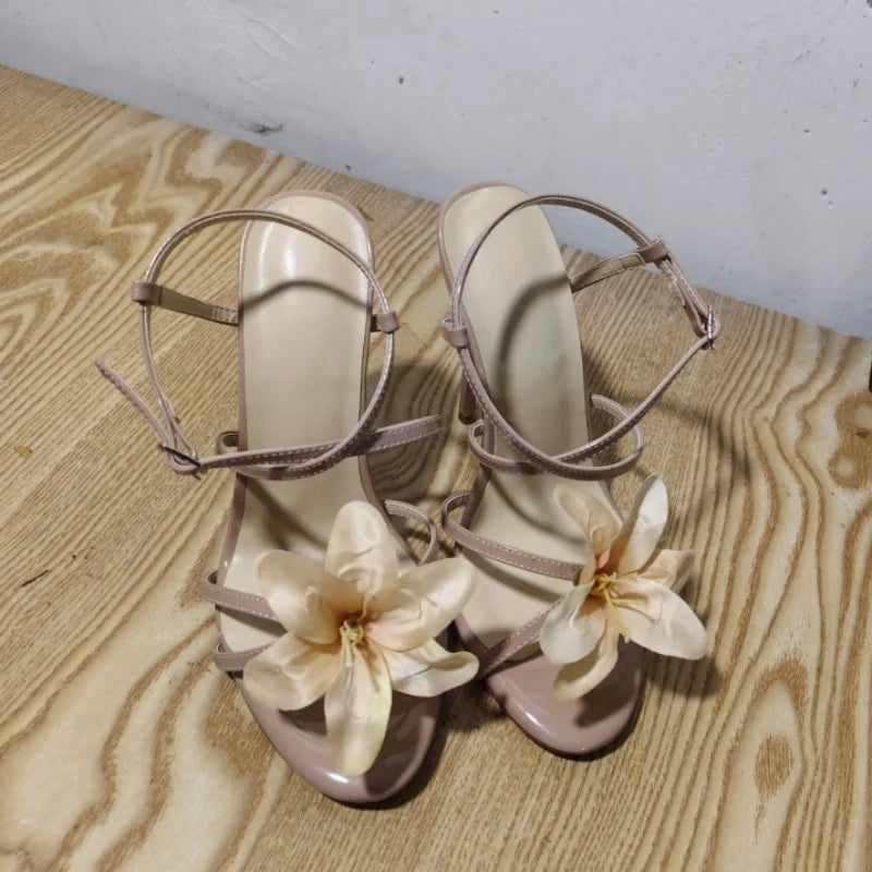 Pair of beige high-heeled sandals with floral decorations on a wooden surface.