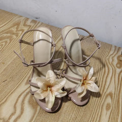 Pair of beige high-heeled sandals with floral decorations on a wooden surface.