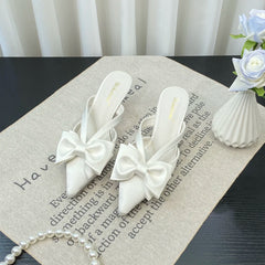 Outdoor chic white bow slip-on shoes displayed for weddings and events on a textured surface with text and a vase of flowers in the background.