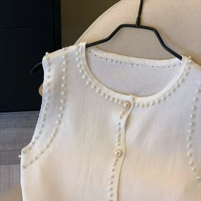 White cardigan with pearl embellishments on a hanger against a neutral background