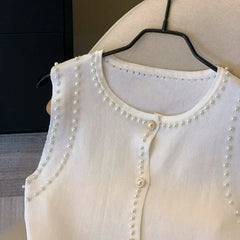 White cardigan with pearl embellishments on a hanger against a neutral background