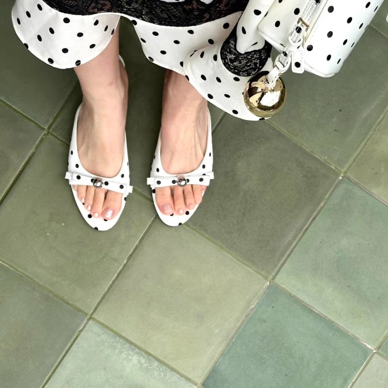 White sandals with black polka dots worn on a tiled floor