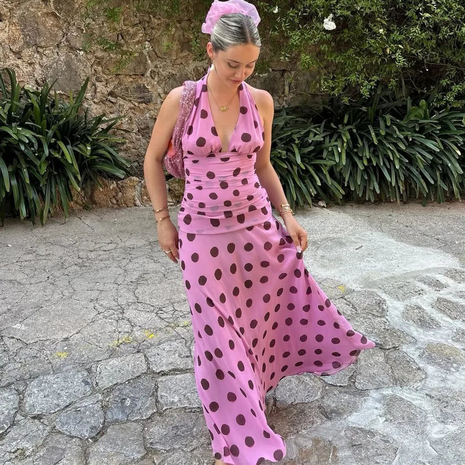 Woman in a pink polka dot dress standing outdoors on a stone path.