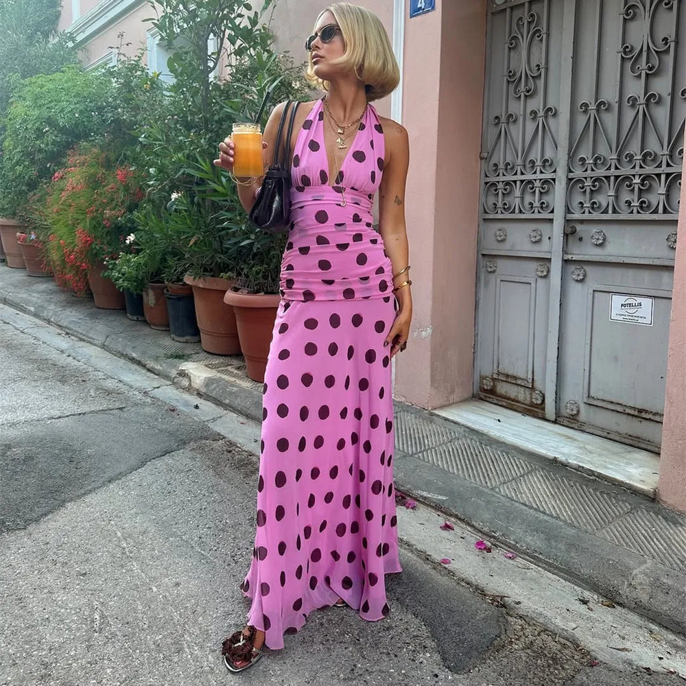 Woman in a pink polka dot dress holding a drink on a street.