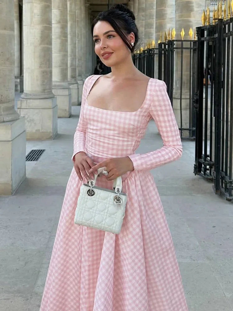 Woman in a romantic cottagecore outfit idea in pink plaidholding a white handbag in an urban setting.