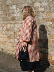 Person wearing a red and white checkered coat against a stone wall.