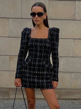 A woman wearing a black and white checkered dress against a stone wall.