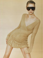 Woman wearing a v-neck long-sleeve mini dress shown with ruched waist and sunglasses against a beige background