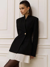 Asymmetric blazer-style mini dress with a sculpted neckline and pleated hem shown in a warm interior setting for a polished city look.