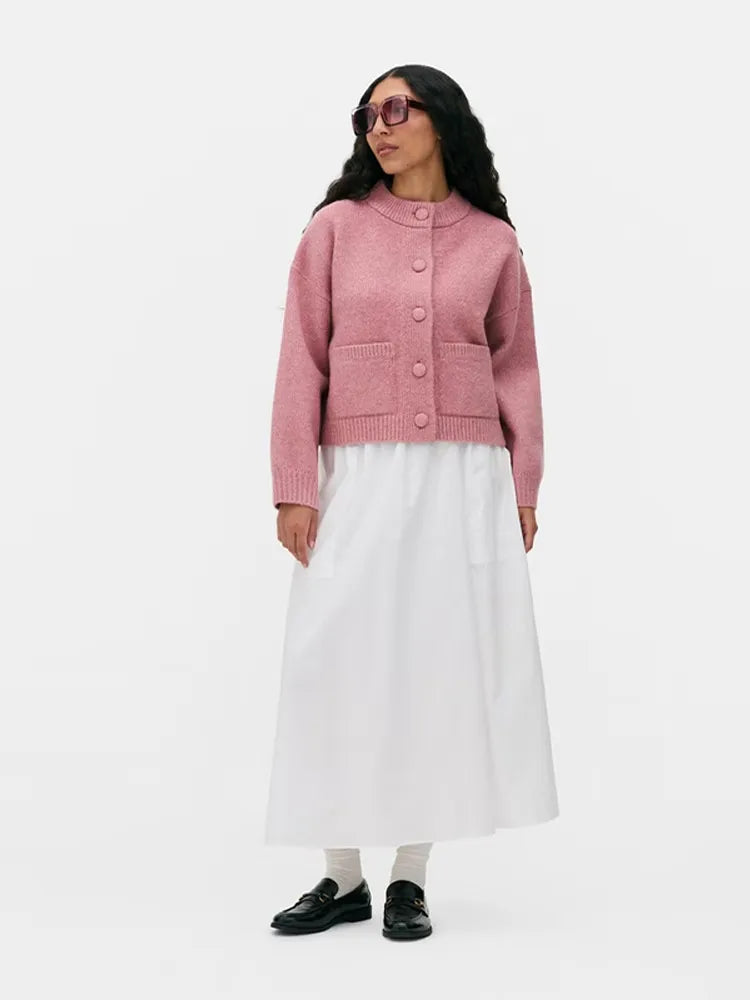 Close-up of the pink knit cardigan highlighting oversized buttons, neat stitching, and the structured patch pocket detail on the front.