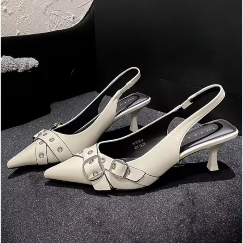 Pair of white pointed-toe kitten heel sandals with buckle strap, kitten heel shoes with buckles on a dark surface.