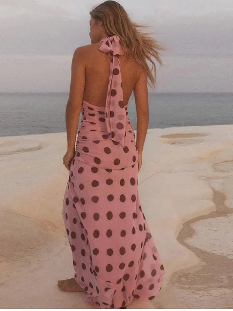 Backless pink maxi dress with polka dots, back view of a woman. standing on a beach