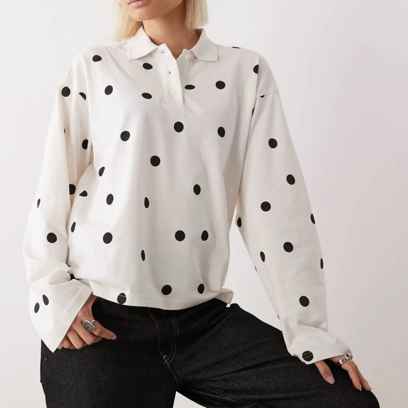 Model wearing a white polka dot long sleeve polo shirt styled casually against a plain studio background.