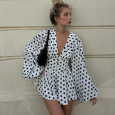 A woman wearing a Polka dot puff sleeve mini autumn dress with a deep V styled for a city look against a beige wall.
