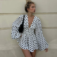 A woman wearing a Polka dot puff sleeve mini autumn dress with a deep V styled for a city look against a beige wall.