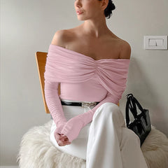 Woman wearing a pink off-shoulder top and white pants sitting on a chair.