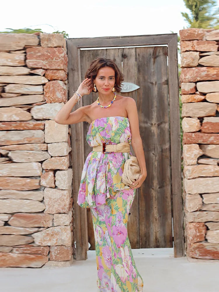 Woman in a floral dress standing in front of a stone wall and wooden door.