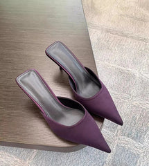 Purple pointed toe high heel mules placed on wooden table