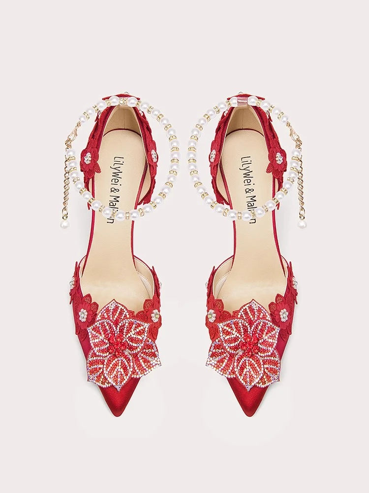 Red high-heeled shoes with floral lace details and pearl straps on a light gray background
