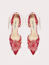 Red high-heeled shoes with floral lace details and pearl straps on a light gray background