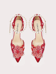Red high-heeled shoes with floral lace details and pearl straps on a light gray background