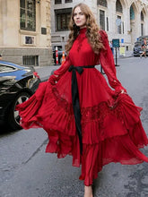 Woman in a red lace evening gown with long sleeves and a waist belt standing on a street.