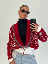 Person taking a mirror selfie wearing a red paisley print cardigan with tassel trim over a black turtleneck and light denim jeans