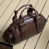 Brown leather satchel handbag with gold hardware on wooden floor