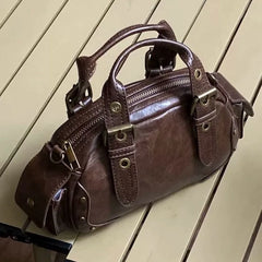Brown leather satchel handbag with gold hardware on wooden floor