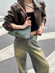A person wearing a vintage denim hobo bag with a brown strap styled for casual wear, holding a blue handbag on a street.