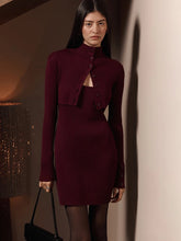 Editorial indoor styling of a ribbed knit mini dress layered with a cropped long-sleeve cardigan and structured handbag.