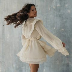 Woman in a butterfly sleeveless summer dress styled in soft natural light against a textured grey wall sideview.