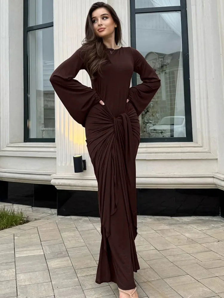 Woman wearing a brown dress standing in front of a building with large windows.