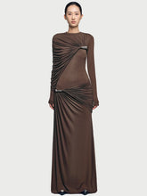 Model wearing a chocolate brown one-shoulder maxi dress with a single long sleeve, standing against a clean studio background.