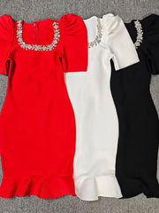Three dresses in red, white, and black with embellished necklines on a gray surface.