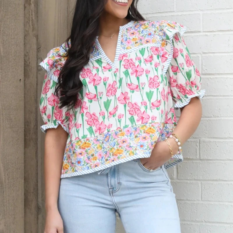 Model wearing a floral print blouse with ruffle shoulders and half puff sleeves styled with light wash jeans for a casual daytime look.