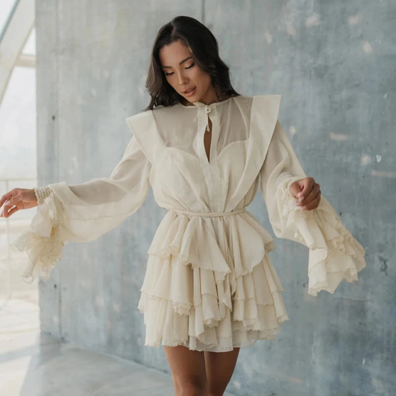 A woman wearing an apricot chiffon mini dress with ruffled layers and a romantic silhouette in a minimalistic setting.
