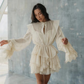 A woman wearing an apricot chiffon mini dress with ruffled layers and a romantic silhouette in a minimalistic setting.